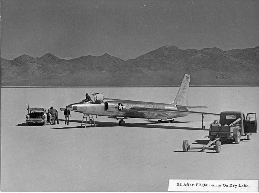 Two pilots standing next to a car and a U-2 aircraft.